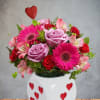 Pink and red flower arrangement in a white heart-decorated vase with a red heart pick