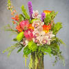 Mixed bouquet with orchids, roses, and green blooms in a glass vase