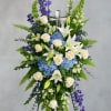 Standing floral spray with white lilies, cream roses, blue hydrangeas, and purple flowers