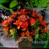Orange and red mixed flower arrangement in a square vase