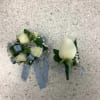 Two white rose boutonnieres with blue ribbon accents on a speckled floor