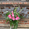 Pink roses arranged in a glass vase with branches and greenery