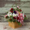 Basket arrangement of red roses, white daisies, and pink carnations with a heart ribbon