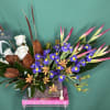 Arrangement of white roses, purple irises, and pink tropical blooms in a rectangular vase