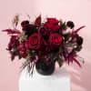 Deep red rose arrangement in a black vase on a white pedestal