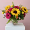 Bright mixed bouquet with sunflowers, gerbera daisies, roses, and a glass vase