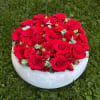 Round arrangement of red roses in a white bowl on grass