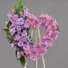 Heart-shaped floral wreath on a wooden stand with pink and purple roses