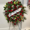 Standing floral spray of red roses and lilies with a white ribbon on an easel