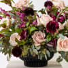Bouquet of pale pink roses and deep burgundy flowers in a black vase