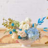 Pastel floral arrangement in a white pedestal bowl with blue accents