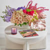 Mixed bouquet of roses and purple flowers in a white vase with a candle