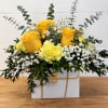 Yellow roses and carnations in a white gift bag with trailing greenery