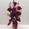 Red roses arranged in a clear glass vase with a burgundy ribbon