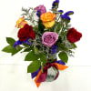Mixed bouquet of red, yellow, and lavender roses with purple filler flowers in a glass vase with colorful ribbons