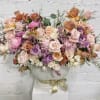 Large pastel rose arrangement in a white vase with a gold ribbon