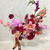 Pink and red mixed flower arrangement in a white vase with a ribbon