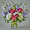 Pink and white roses with lavender blooms in a clear glass vase