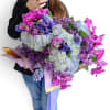Large bouquet of purple orchids, hydrangeas, and mixed blooms wrapped in lavender paper