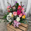 Mixed bouquet of pink, white, yellow, and purple flowers in a glass vase with a pink ribbon