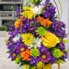 Bright mixed bouquet in a yellow mug-style vase with purple, yellow, orange, and white flowers.