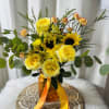 Yellow roses and sunflowers in an amber vase with orange ribbon