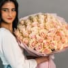 Woman holding a large bouquet of pale pink roses wrapped in pink paper