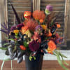 Colorful floral arrangement in a black vase with orange roses and purple blooms