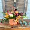 Autumn floral arrangement in a pumpkin-shaped container with orange, pink, and burgundy blooms
