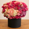 Large round bouquet of pink, peach, and lavender roses in a black box