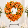 Orange floral wreath on a black stand with roses and lilies