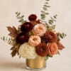 Autumn floral arrangement in a gold vase with a small pumpkin centerpiece