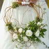 White floral wreath with green foliage and twisting branches held by a person