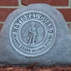 Gray memorial stone with a National Guard emblem against a brick wall