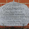 Gray memorial stone engraved for grandmother against a brick wall
