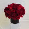 Compact arrangement of red roses and carnations in a black vase on a clear cube stand