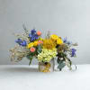 Colorful bouquet in a white floral vase with yellow, blue, pink, and green blooms