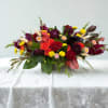 Low floral centerpiece with red roses, calla lilies, and yellow accents in a wooden container