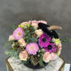 Pink and cream flowers arranged in a black vase with a dark feather accent.