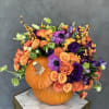 Orange pumpkin centerpiece with purple and orange flowers