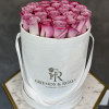 Pink roses arranged in a white round hat box with ribbon handles