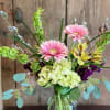 Tall mixed bouquet with pink gerbera daisies, green hydrangeas, and yellow blooms in a clear glass vase.