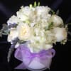 White floral bouquet in a white vase with a purple ribbon