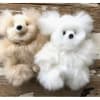 Two fluffy teddy bears, one beige and one white, on a wooden surface.