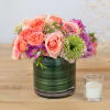 Pink and purple roses arranged in a glass vase beside a small candle