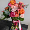 Bouquet of pink and orange roses in a glass vase with a pink ribbon