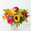 Mixed bouquet of lilies, roses, and a sunflower in a clear glass vase