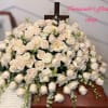 Large spray of ivory roses on a wooden casket with a cross at the back