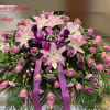 Large pink and purple lily and rose spray with bow and palm fronds on a stand