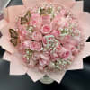 Round bouquet of pink roses and white filler flowers with gold butterfly accents wrapped in pale pink paper.